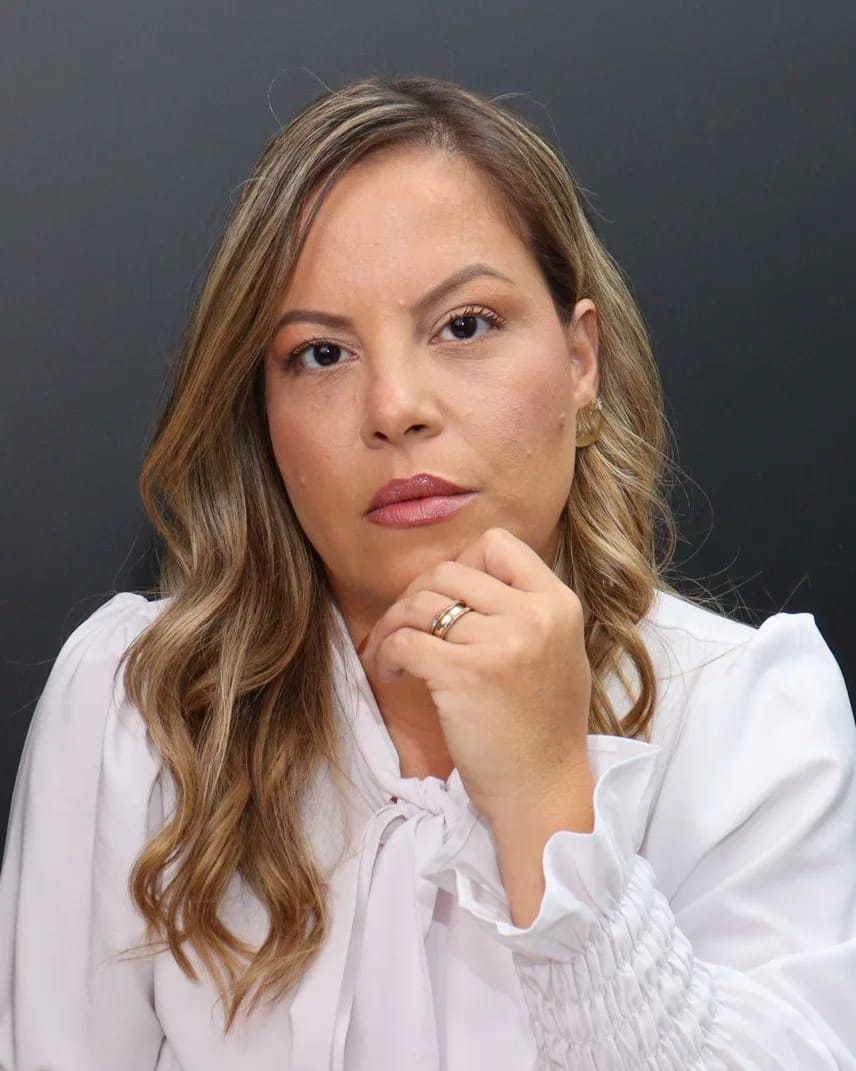 Carol Lorena, com a mão no queixo, olhando para a câmera
